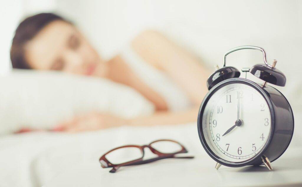 young woman sleeping while lying in bed comfortably and blissfully on the background of alarm clock